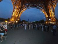 In der Nacht am Eiffelturm viele Touristen, im Hintergrund das Hochhaus von Montparnasse