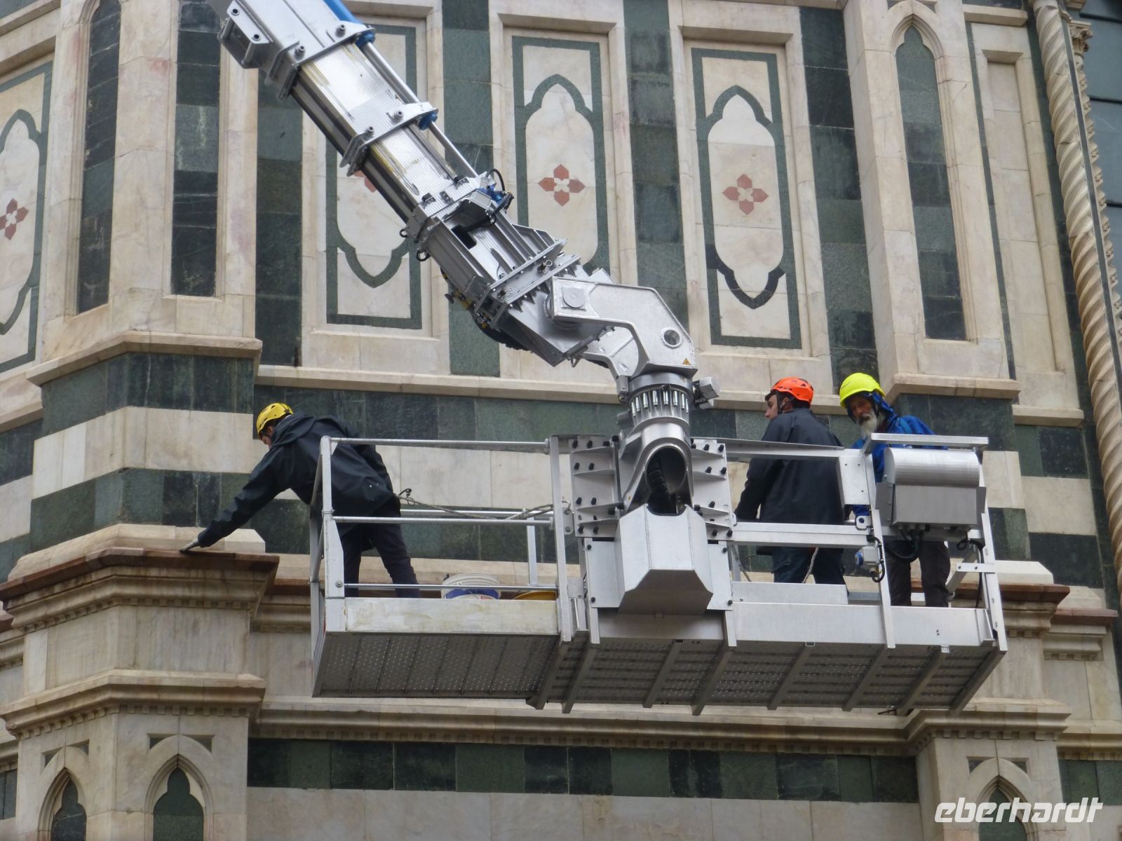 Hält die Fassadenverkleidung? Drei Männer prüfen mit einem Stock ihre Haltbarkeit.