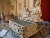 Ein geöffneter römischer Sarkophag. Im Hintergrund eine erhaltene Badewanne aus der Antike