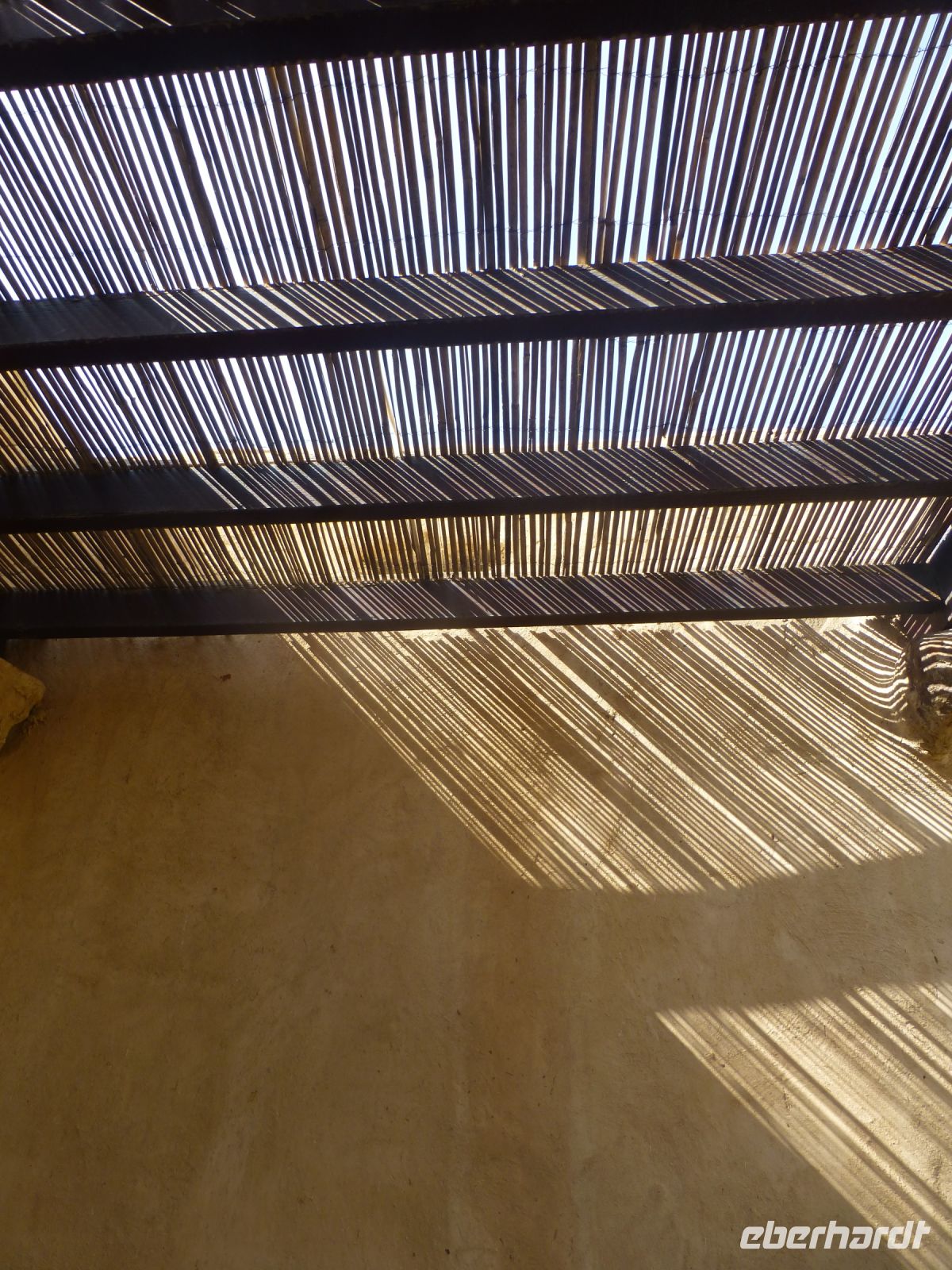 Der Sonnenschutz aus Schilf zeichnet ein feines Muster auf die Wand.