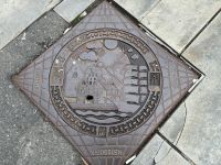 Gullydeckel in Bergen mit historischer Stadtansicht