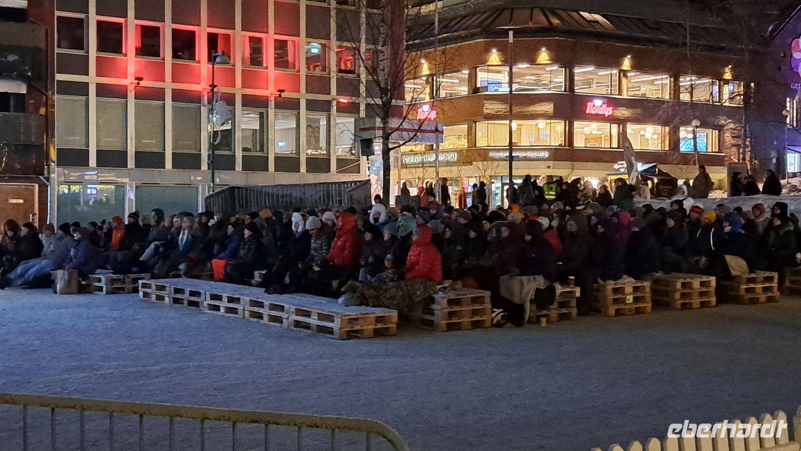 Tromsø - Friluftsliv - Freiluftleben - Filmfestival mitten im Winter auf dem Hauptplatz auf Rentierfellen sitzend
