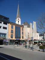 Eine moderne Einkaufshalle und im Hintergrund die Stadtkirche von Bad Ischl.